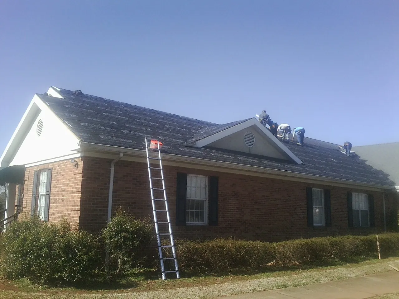 Crew tearing shingles off a brick ranch roof with a ladder set — Metal Roof Repair work by our crew in Farmdale