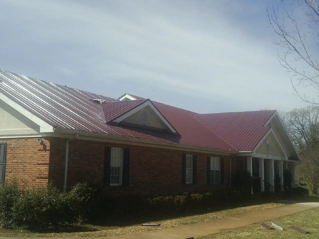 Red metal roof with gabled entries on a long brick building, from a Hail Damage Roof Repair job in Farmdale
