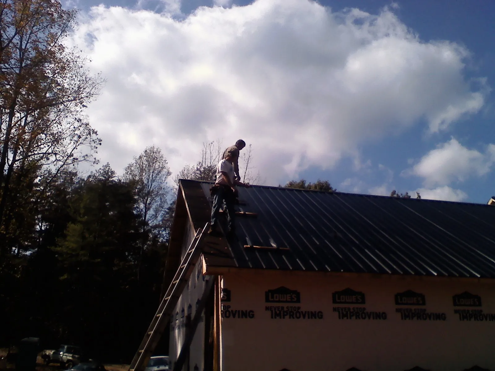 Roofer fastening dark metal panels high against a cloudy sky, from a Roof Inspection job in Farmdale