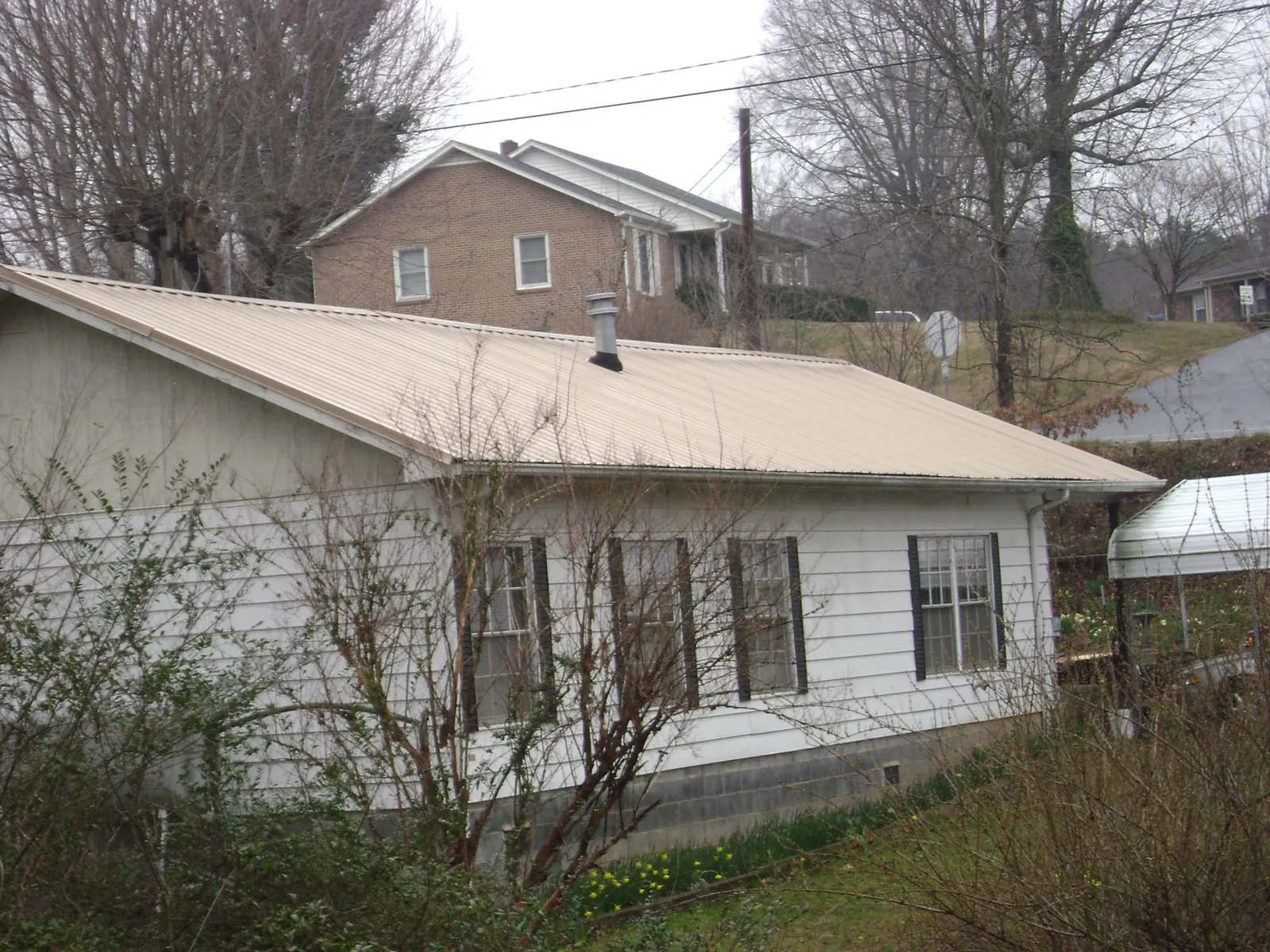 Tan metal roof on a white sided house set into a hillside — Commercial Roofing by Roofing Brothers in Farmdale
